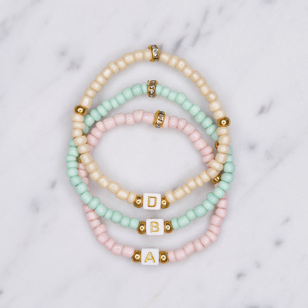 beaded painted pastel pink cream green block cubic initial gold letter colour personalised custom bracelet gold accents 3 bracelets on marble
