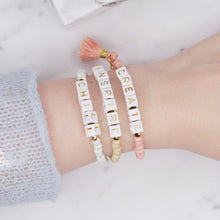 Load image into Gallery viewer, 24k gold plated beaded cubic building block letter initial beads charm tassel painted pink beige biscuit white shimmer elastic stretchy gold bracelets create chill inspire affirmation on wrist