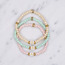 Load image into Gallery viewer, beaded painted pastel pink cream green block cubic initial gold letter colour personalised custom bracelet gold accents 3 bracelets on marble
