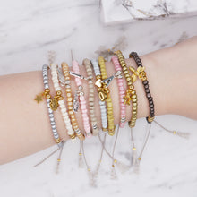 Load image into Gallery viewer, beaded tie up square knot nylon polyester cord grey pink blue cream white olive green metallic antique gold bronze silver tan charm bracelets with tassels friendship bracelets on marble labelled names on wrist
