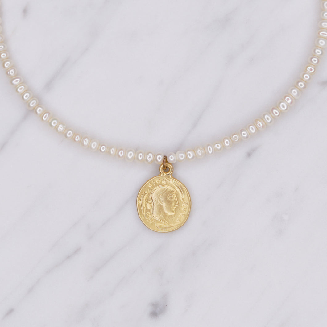 button pearls and matte gold plated greek pendant head double sided coin necklace close up on marble