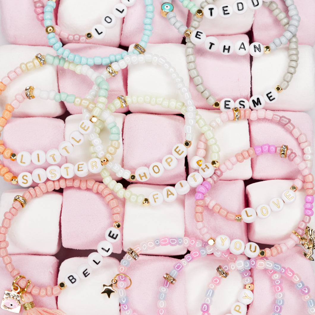 colourful stretch elastic bracelets on pink and white marshmallows name bracelets gold charms feature accent beads acrylic letters pink blue green grey unicorn multi colour